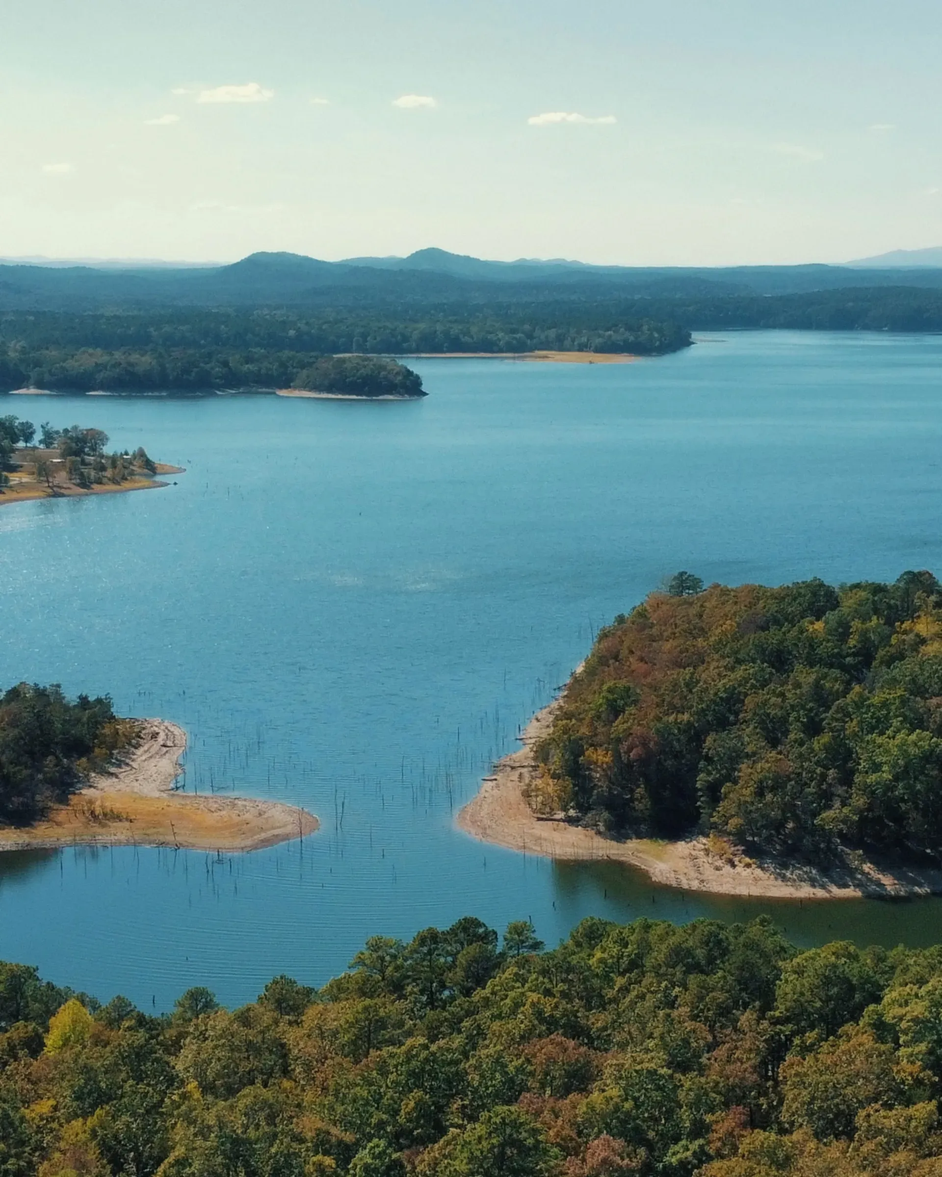Aerial view of Lake Ouachita in early fall, with sandy points and blue coves surrounded by changing trees and mountains beyond